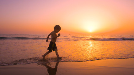A little boy enjoying and playing in the beach at sunset