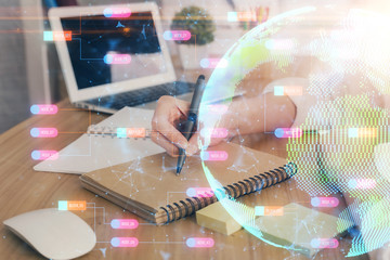 Double exposure of hands making notes with world map hologram and data theme icons. Concept of international network data.