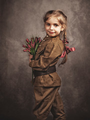 Girl in military retro uniform holds flowers.