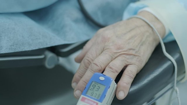 Old patient with pulse oximeter on finger for monitoring during surgery in hospital