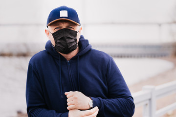A concerned man in a dark blue hoodie with a protective medical mask on his face waiting for the results of a virus test outdoors. Coronavirus pandemic situation.