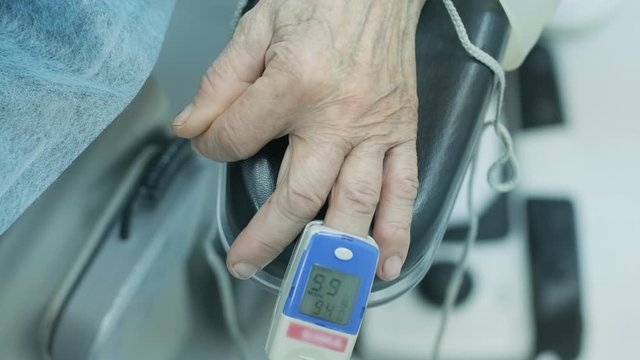 Old patient with pulse oximeter on finger for monitoring during surgery in hospital