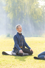 Naklejka na ściany i meble A young man meditates outdoors in a park. 