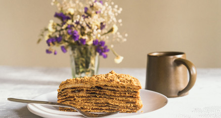 Sweet delicious piece of layerd honey cake on a plate with a cup of tea or coffe on the table
