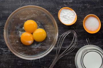 Top view of bowl with three yolks, starch, sugar and milk and whisk as ingredients to make custard...