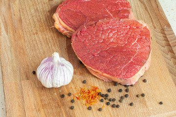 Raw beef steaks on a wooden board with garlic, black pepper and saffron. Delicious lunch concept