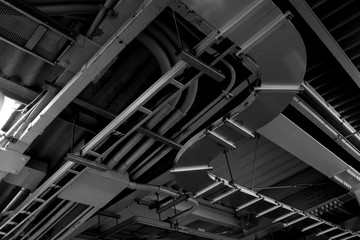 Monochrome photo of power distribution and plumbing equipment installed on the ceiling of an...