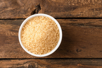 Brown cane sugar in bowl on rustic wooden table. Top view