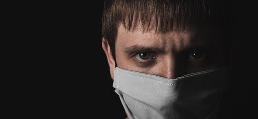 Face of man in medical protective mask, close up view on black background. Concept,problem and risk of coronavirus pandemic. COVID-19. Self isolation. Immunity fight,survival. World biological hazard.