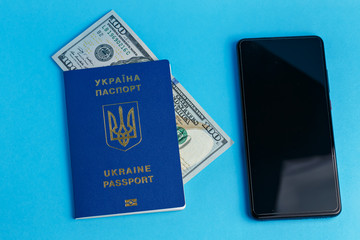 100 dollars banknote inside one Ukrainian foreign passport on a blue background close-up traveling business near phone businessman
