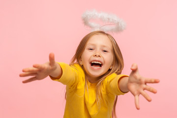 Delighted happy little girl with angelic halo screaming with happiness and reaching into camera to...