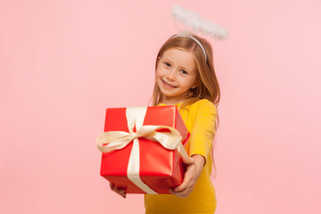 Portrait of charming kind little ginger girl with freckles and angelic halo holding big gift box, congratulating on holiday and giving birthday present. indoor studio shot isolated on pink background