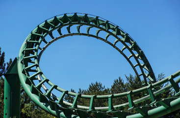 Curved Rollercoaster at a theme or amusement park empty green metal tracks and on blue sky...