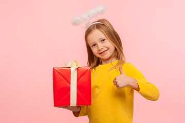 Portrait of nice kind little ginger girl with freckles and angelic halo over head holding gift box...