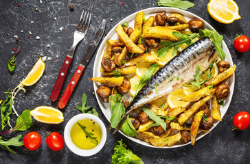 Baked mackerel with lemon, baked potatoes and mushrooms on a plate on black stone background.