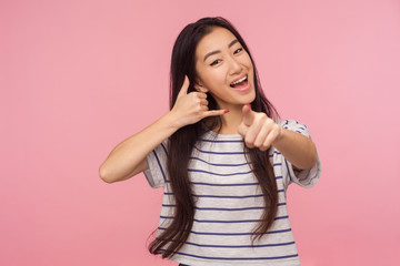 Hey you, let's communicate! Portrait of happy girl with long brunette hair making call me gesture with hand shaped like telephone and pointing to camera, showing dial my number. studio shot isolated