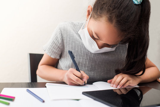 Distance learning online education during the epidemic of coronavirus Covid-19. A girl in a protective face mask does homework for school during quarantine.