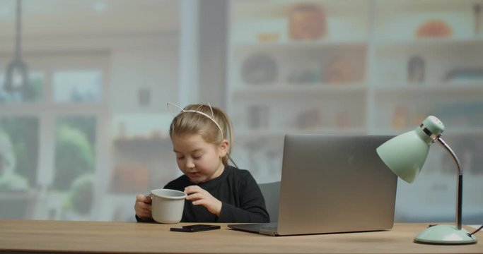 Five year old girl typing on the computer behind the desk in a cosy living room. slow motion 4K. 