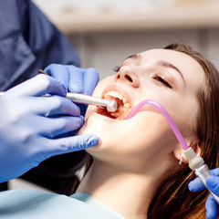 Dentist treating teeth to young woman patient in clinic.