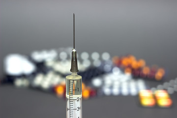 Medical syringe with a needle and colorful pills capsule on background.