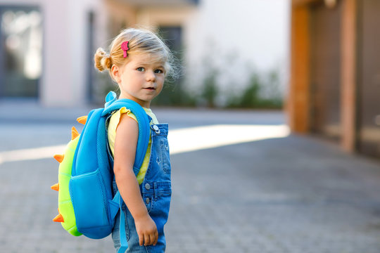Cute little adorable toddler girl on her first day going to playschool. Healthy beautiful baby walking to nursery school and kindergarten. Happy child with backpack on the city street, outdoors.