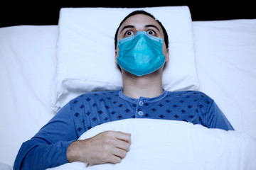 Portrait of an insomniac man trying to sleep while wearing a mask, coronavirus quarantine concept