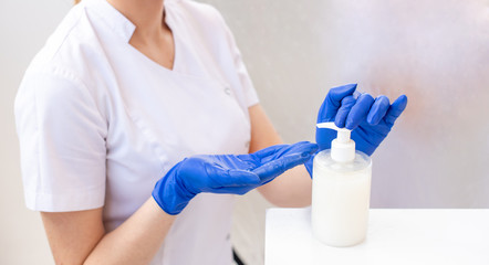 Hands of a female doctor in blue gloves using gel for disinfection of viruses