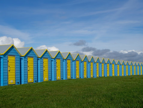 Colourful line of beach huts with grass and blue sky. No people.