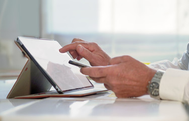 tablet and mobile phone held by man in white shirt - doctor or businessman while analyzing data online.