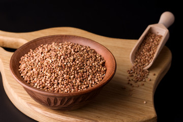 buckwheat in a clay bowl on a wooden plank on a black background