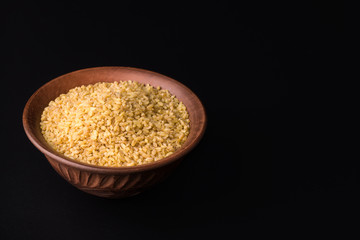 raw bulgur in a clay bowl on a black background. copy space