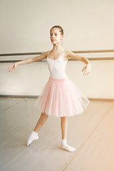 Little cute girl in pink skirt making ballet movement at dance studio