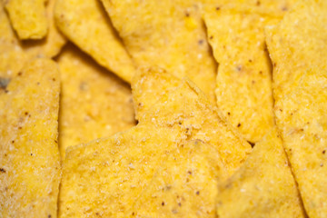 Nachos on a wooden board, close-up. Harmful Mexican snack, unhealthy fast food. Crispy, salty yellow corn triangles