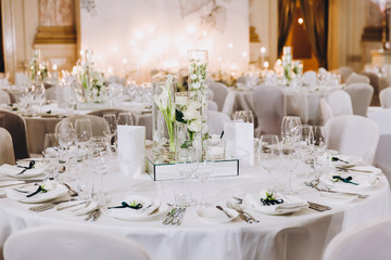 Wedding decorations. On the tables in the banquet hall are compositions of vases with water and white flowers, plates with napkins, candles and glasses