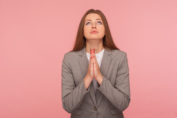 Please, god help! Portrait of imploring young woman in business suit looking up and praying, begging with obedient pleading expression, gesture of asking apologizing. indoor studio shot, isolated