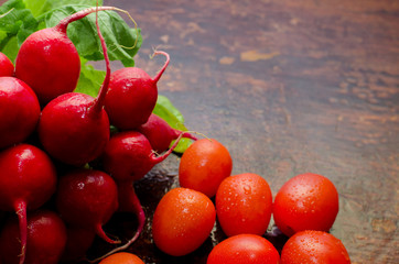radish with green tops and cherry tomatoes on a dark wooden table, vegetable composition, drops of water on vegetables, close-up, space for text