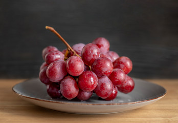 Top view of grapes with water drops in gray plate on wooden table. Bunch of fresh red grapes.