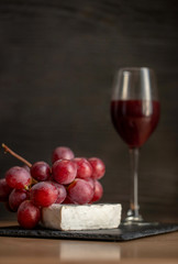 Glass of red wine with grapes and brie cheese on a wooden background. Red Wine bottle, brie cheese and wineglass on black wood background, top view, copy space.