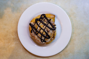 Cinnabon. Cinnamon roll decorated with chocolate on a white plate on blue and yellow background