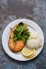 fried salmon with salad, lemon and boiled rice on white plate