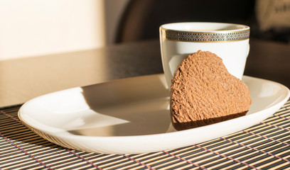  On a white rectangular saucer is a heart shaped chocolate cookie and a cup of coffee with foam.