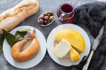cheese on white plate and olives, bread, knife on ceramic background