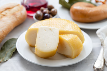 cheese on white plate and olives, bread, knife on ceramic background