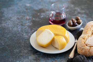 cheese on white plate and olives, bread, knife on ceramic background