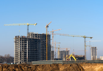 Tower cranes constructing a new residential building at a construction site against blue sky. Renovation program, development, concept of the buildings industry.