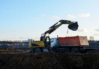 Excavator with a large iron bucket on a construction site during road works. Backhoe dig the ground for the foundation, laying storm sewer pipes. Installation of water main systems.
