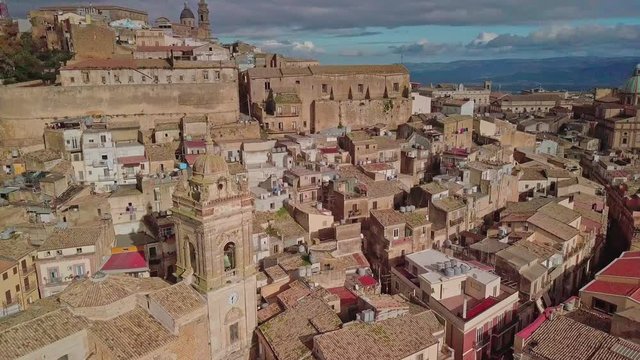 Aerial footage of medieval city of Caltagirone. Drone rotates around old citadel, historic buildings and church, tilting up.
