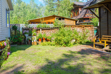 Garden buildings in the country. Shed with a canopy, bench and a street lamp and stack of the firewood over red currant bushes. Country house on the background
