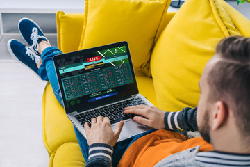 Cropped shot of a man lying on sofa making bets online at bookmaker's website using laptop