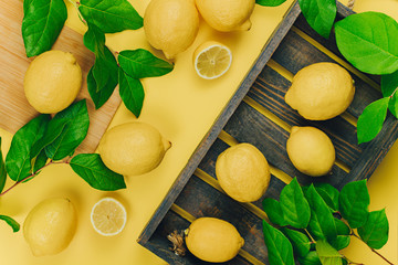 Ripe juicy lemons, green leaves on bright yellow background. Lemon fruit, citrus minimal concept, vitamin C. Creative summer minimalistic background. Flat lay, top view, copy space